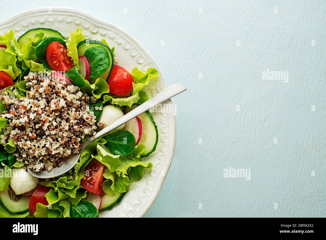 Healthy Green salad with fresh vegetables and quinoa seeds on blue table background Stock Photo