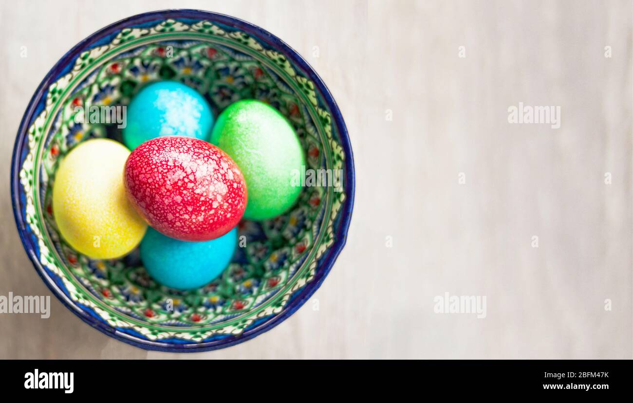 Colorful Easter eggs in bowl on white natural wooden background. Top view. Flat lay. Stock Photo