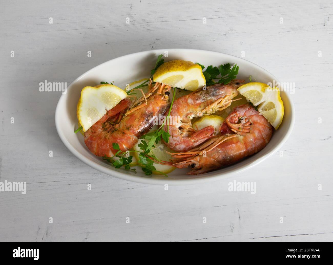 roasted prawns with lemon slices on a white plate and black background Stock Photo
