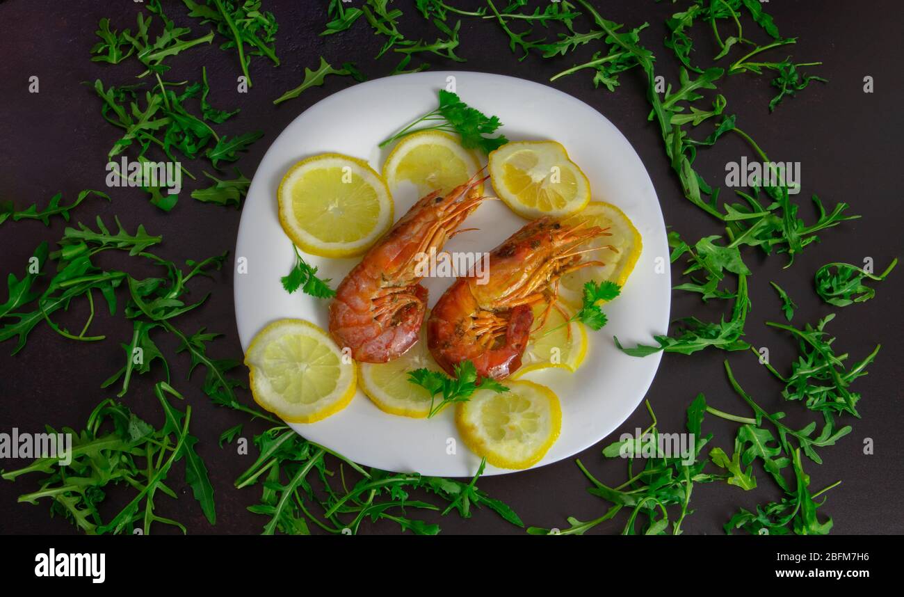 roasted prawns with lemon slices on a white plate and black background Stock Photo