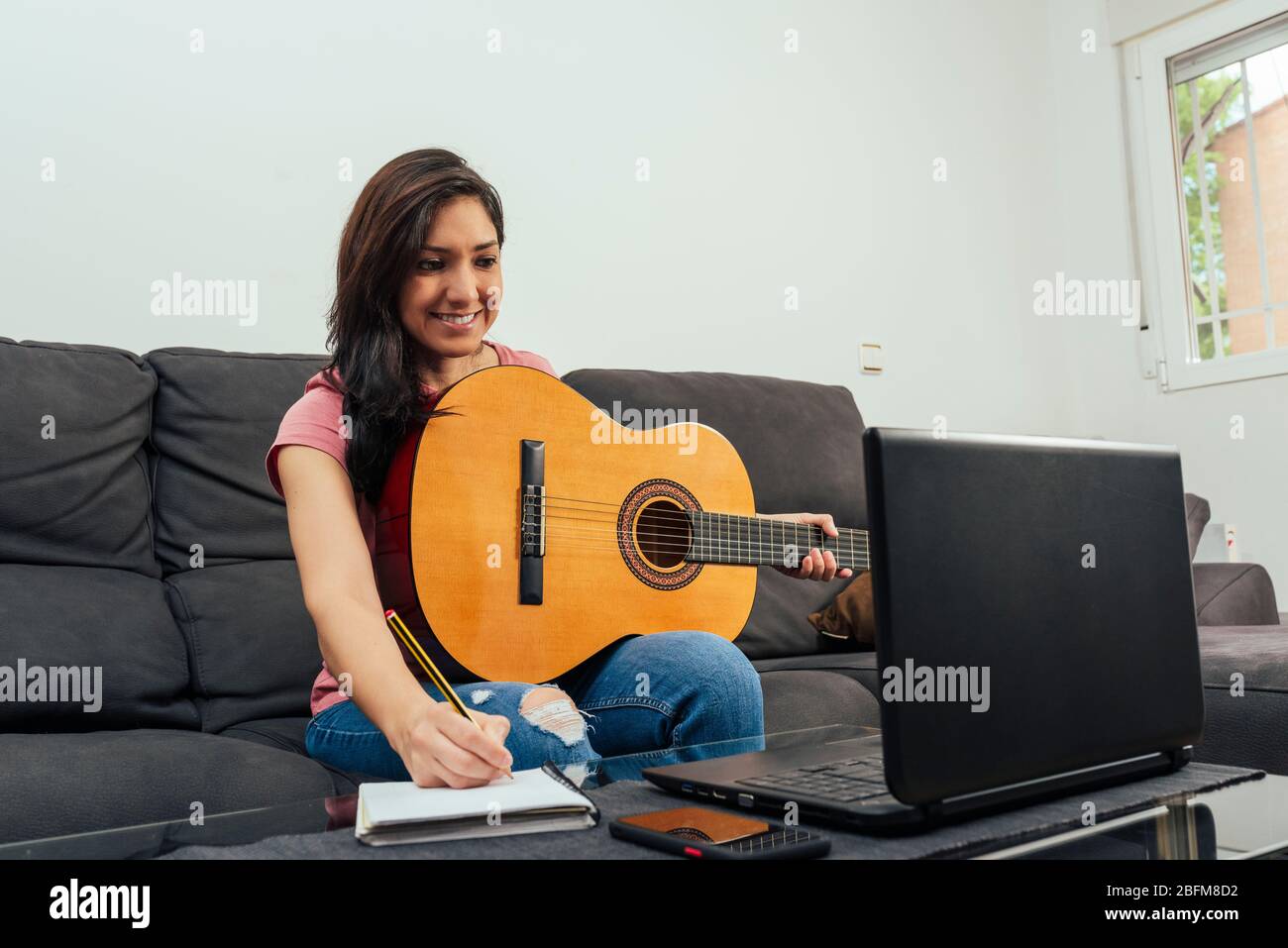 Woman taking guitar lesson notes online. Online learning concept. Stock Photo