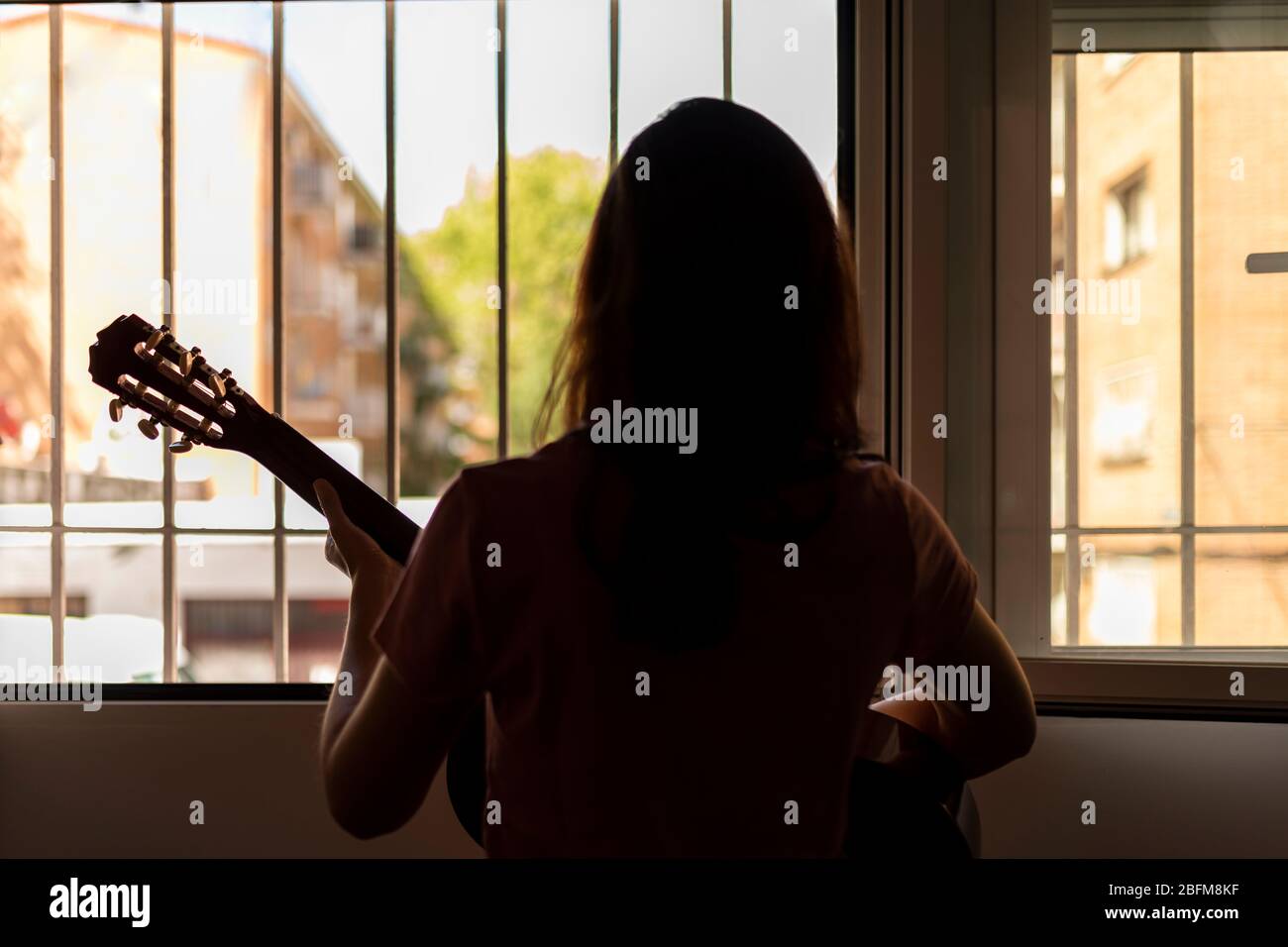 woman on her back playing guitar for her neighbors through the window. Concept of loneliness in confinement. Stock Photo