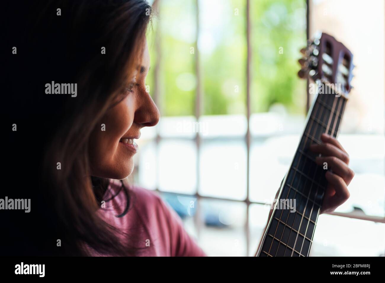 woman playing guitar for her neighbors through the window. Concept of loneliness in confinement. Stock Photo