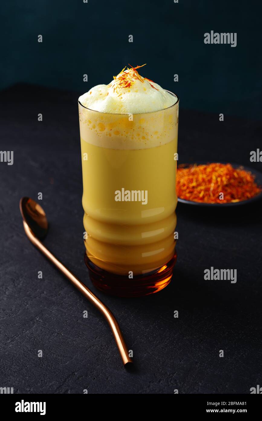 Saffron latte in a glass cup on concrete background,metal straw,dry