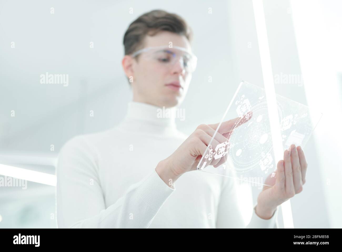 Hands of young contemporary app developer in white jumper and smart goggles pointing at display of transparent futuristic mobile gadget Stock Photo
