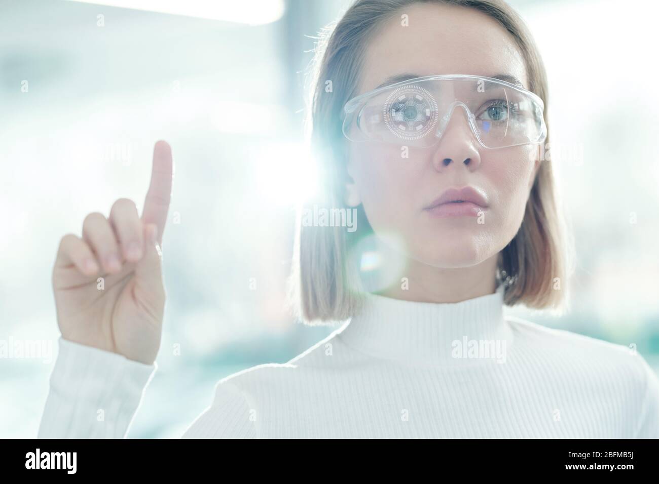 Pretty young female technology developer in smart eyeglasses pressing virtual button on display while making presentation Stock Photo