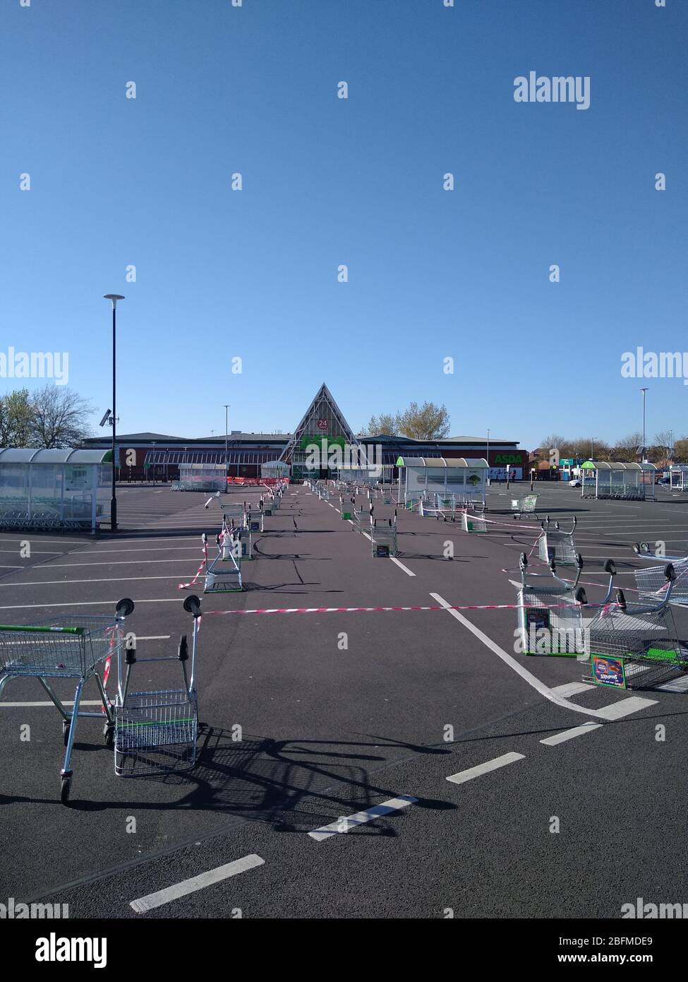 An ASDA supermarket in St Helens, UK uses a line of trolleys/carts in its car park to keep customers socially distanced due the COVID-19 virus. Stock Photo