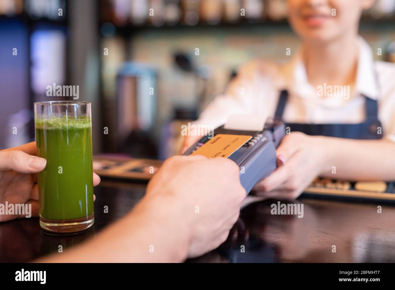 Contemporary client holding plastic card over screen of payment terminal while paying for glass of vegetable smoothie in cafe Stock Photo