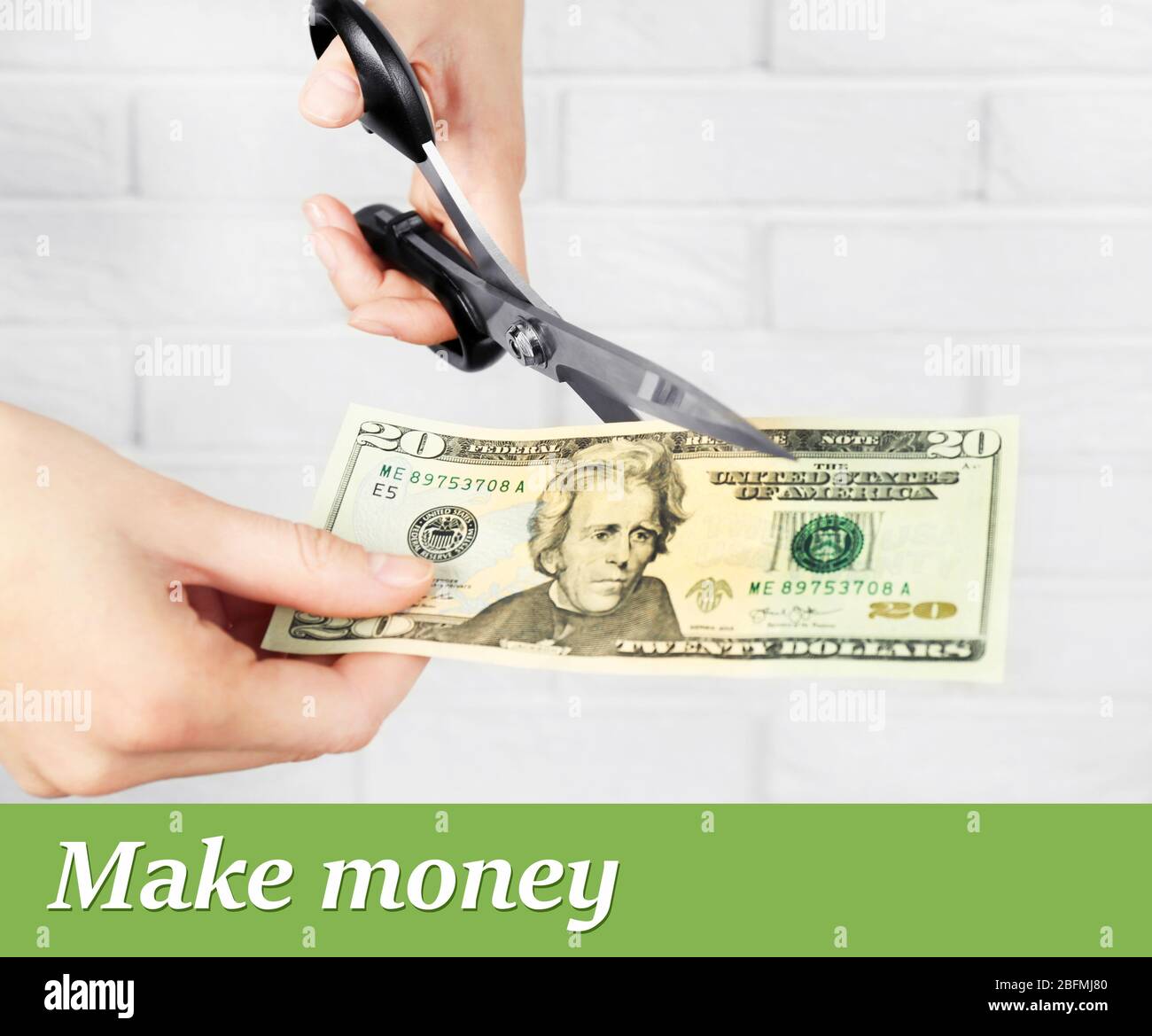 Hands with scissors cutting money on white brick wall background Stock