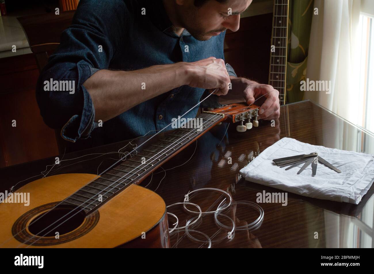 Focus man changing the strings of a guitar at home. Wooden table with