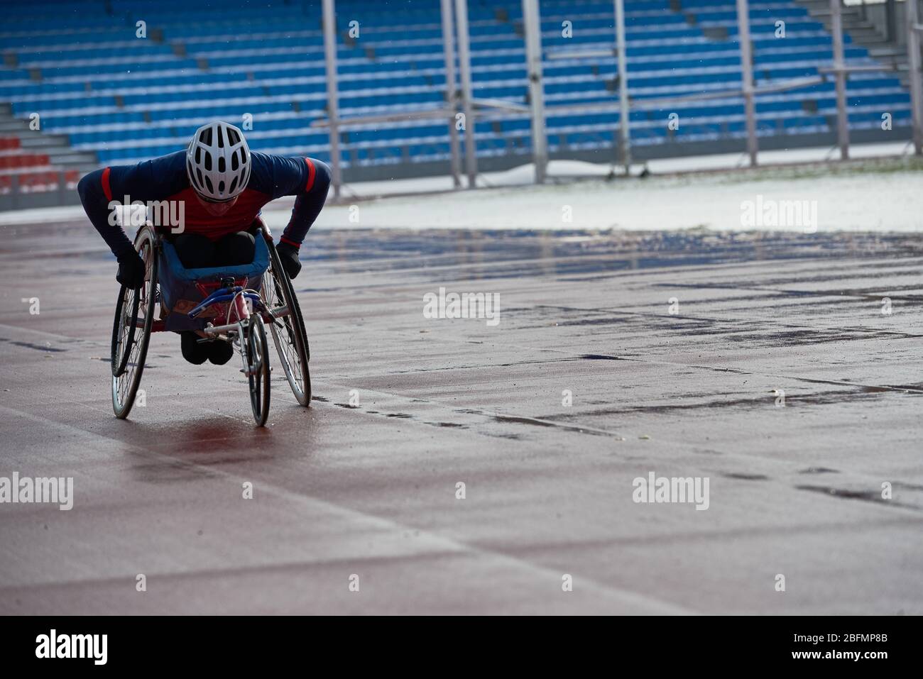 Preparing for wheelchair marathon. Determined paraplegic sportsman racing in handcycle at outdoor track and field stadium in gloomy rainy afternoon Stock Photo