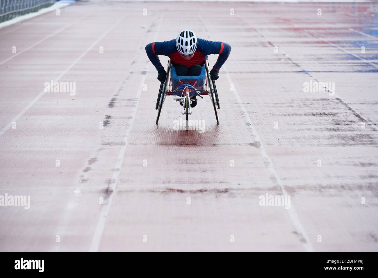Preparing for Paralympics. Determined wheelchair racer in sportswear and helmet reaching finish line while training at outdoor track and field stadium Stock Photo