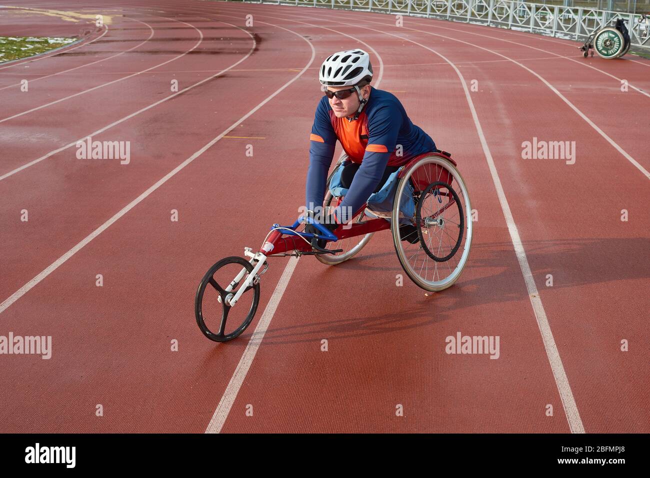 Handicapped sportsman in helmet and sunglasses sitting in racing wheelchair at outdoor track and field stadium and getting ready for marathon Stock Photo