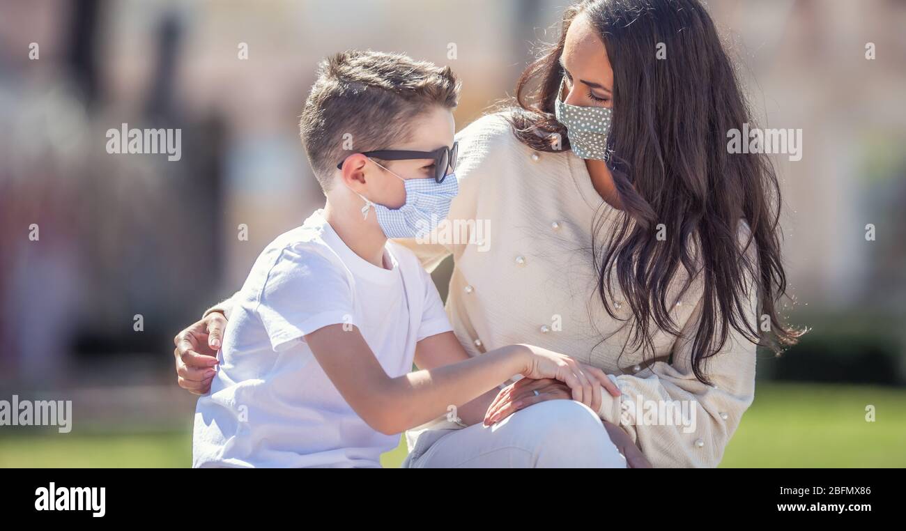 Single mom is looking worried at her son in sunglasses outside, both wearing face masks. Stock Photo