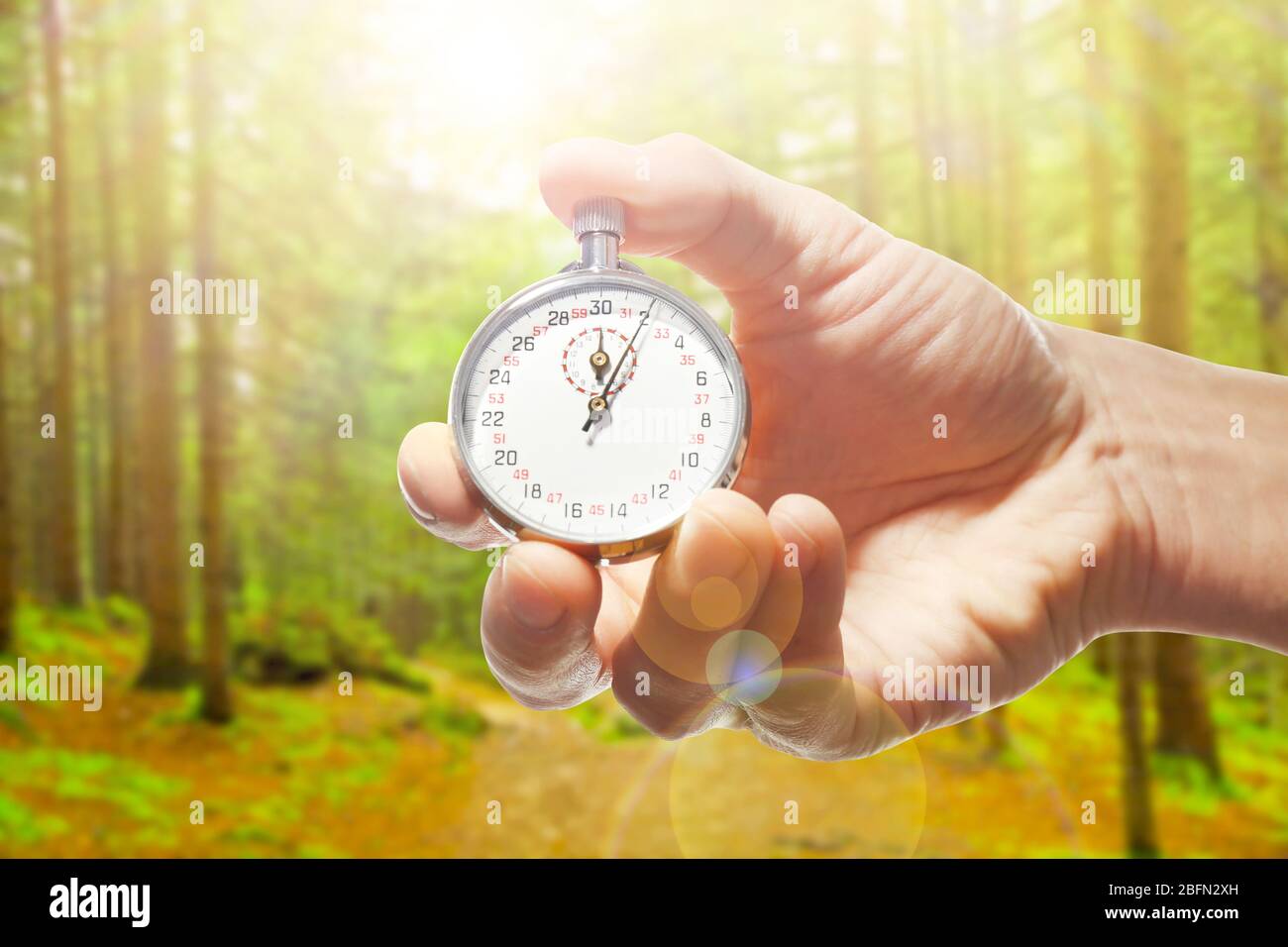 Man holding stopwatch against forest background.Time concept Stock Photo
