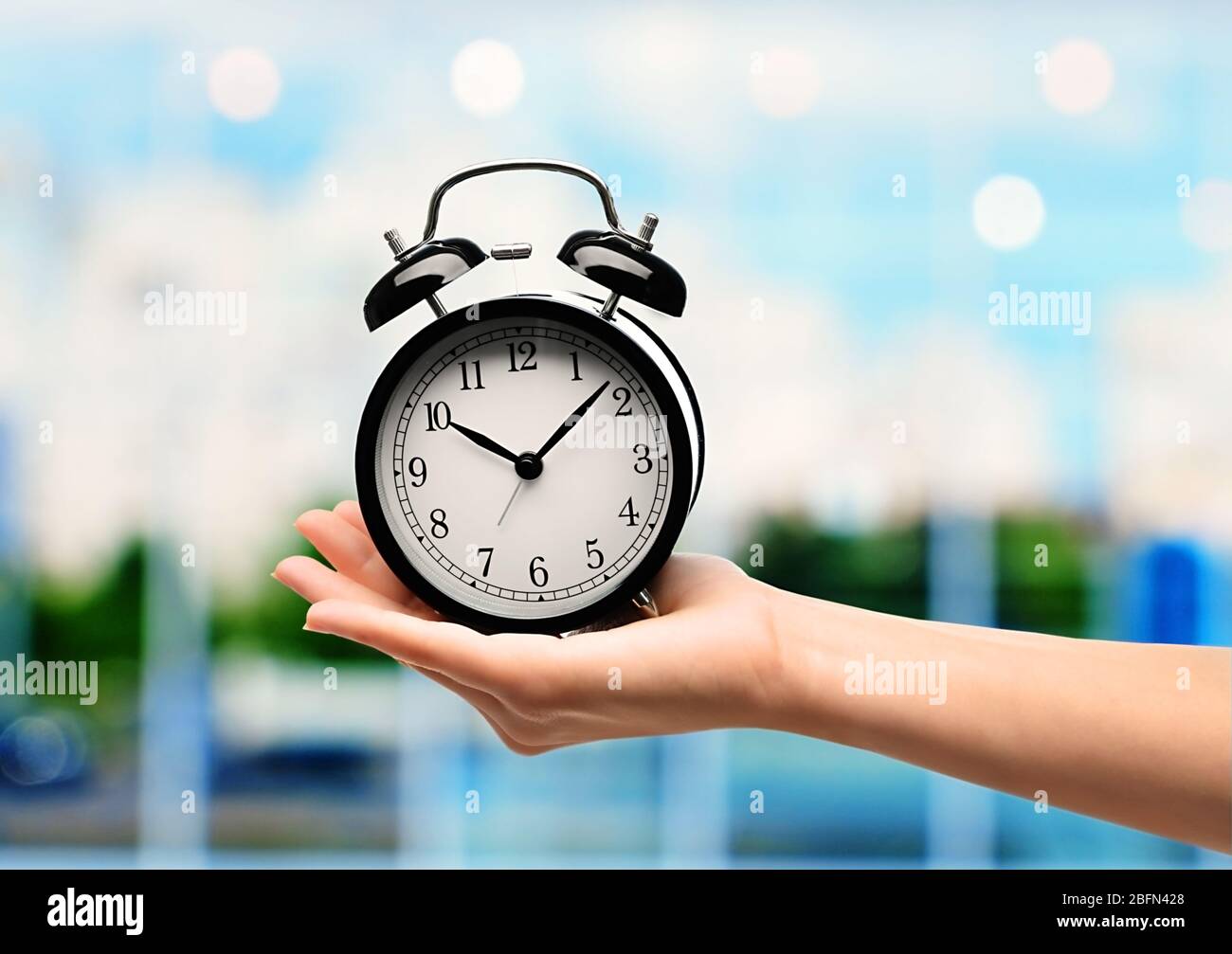 Female hand holding old clock in hand on blurred background Stock Photo