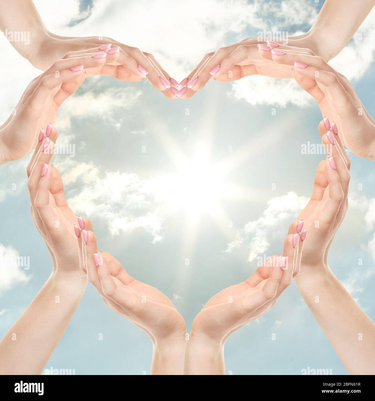 Female hands in heart shape on blue sky background with sun Stock Photo ...