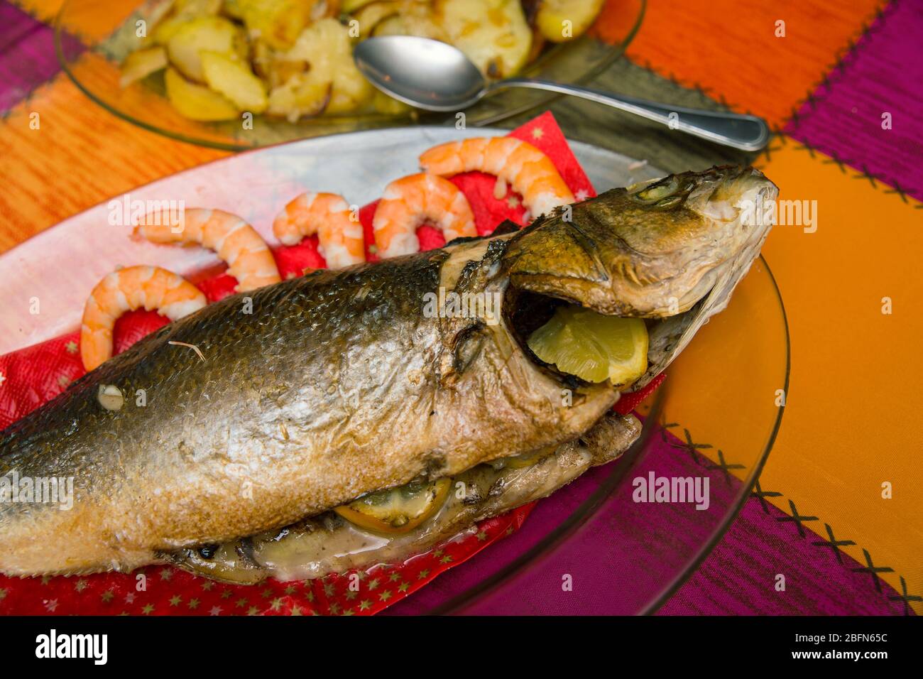 cooked sea bass on a glass dish and a plate with baked potato garnish Stock Photo