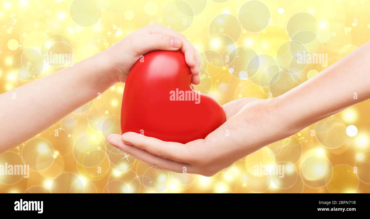 Female and child hands holding red heart on blurred background. Family ...