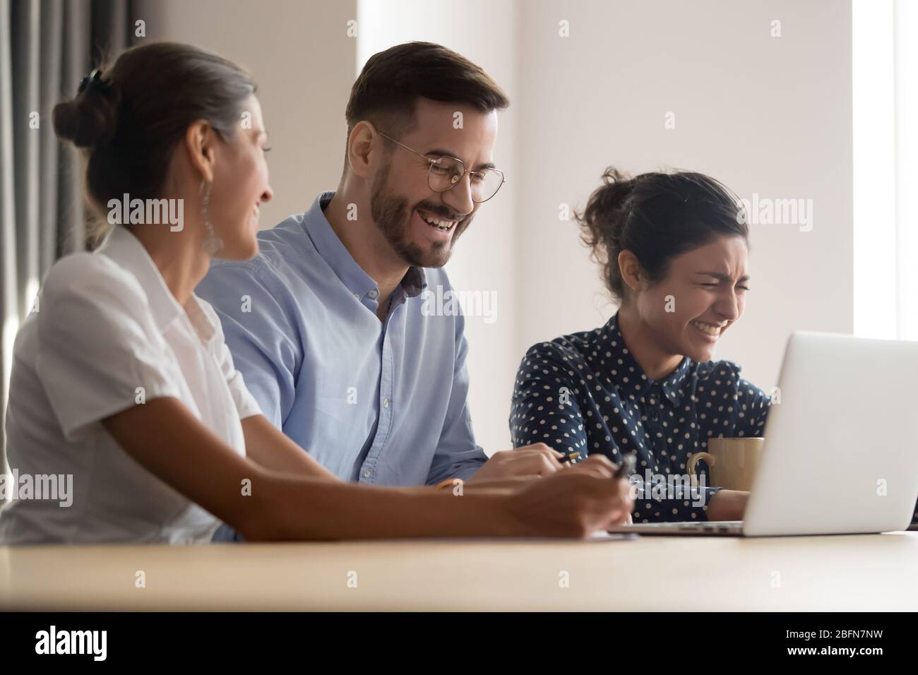 Diverse colleagues feels overjoyed laughing sit at workplace Stock Photo