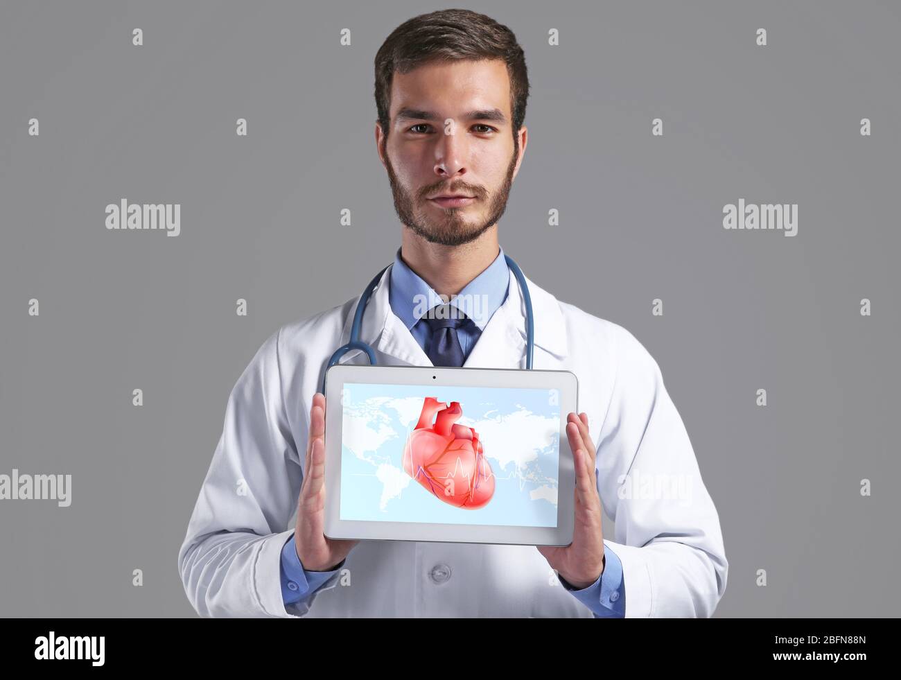 Cardiologist holding tablet with heart on screen against gray ...