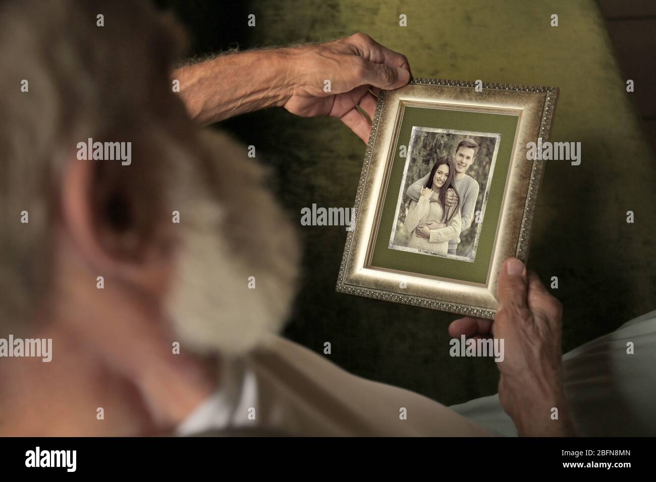 Elderly man holding photo frame with picture of young couple. Happy