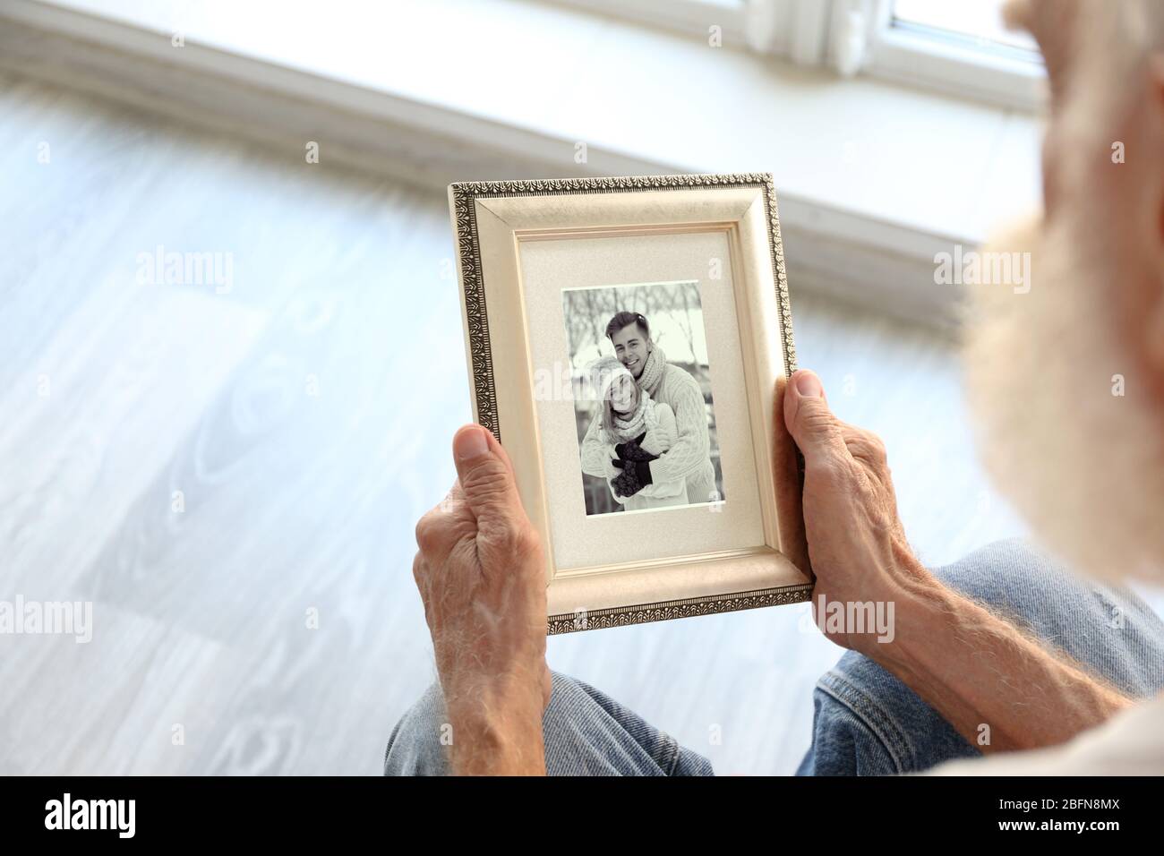 Elderly man holding photo frame with picture of young couple. Happy