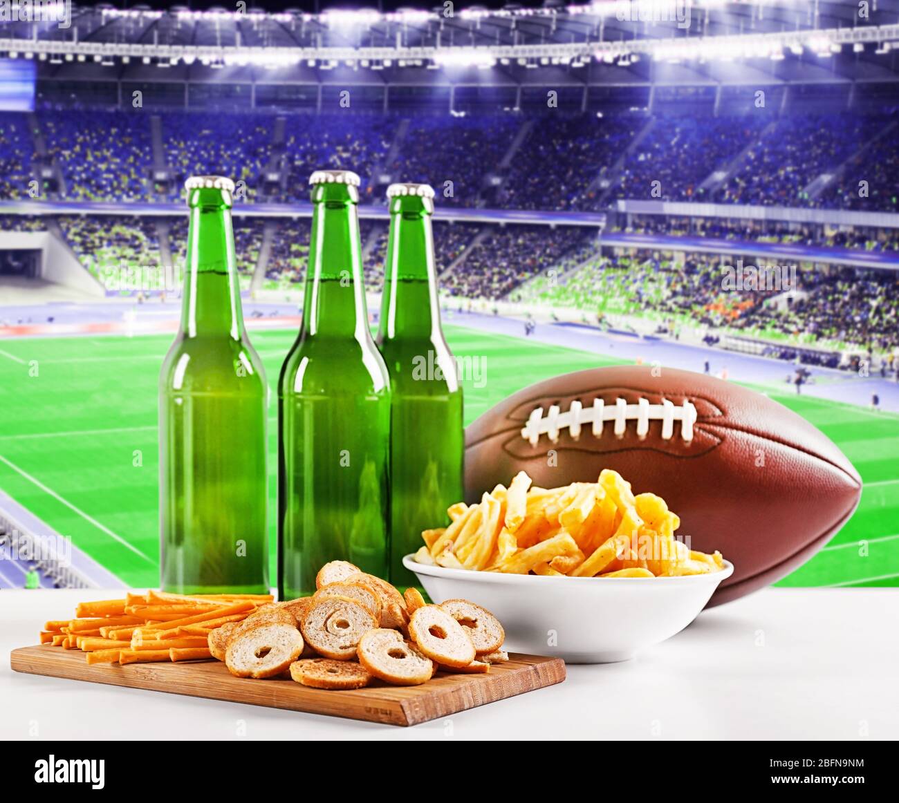 Beer with snack and ball on table against football field background. Sport and entertainment