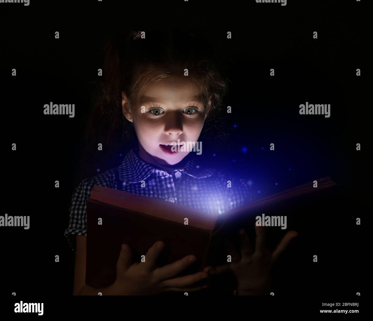 Cute girl reading book at night. Magic light coming out of book. Stock Photo