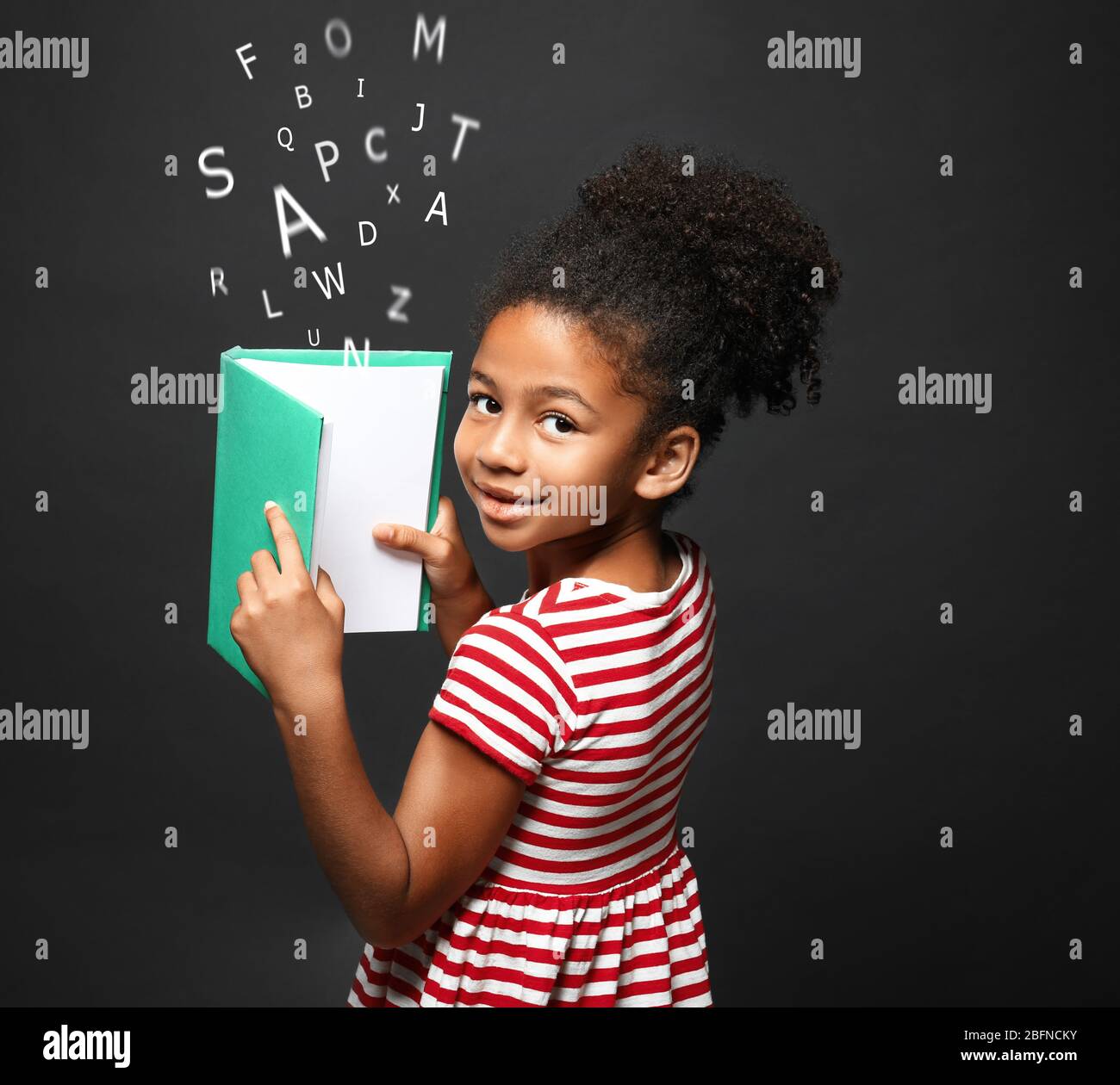 African-American little girl with book and alphabet letters on dark ...