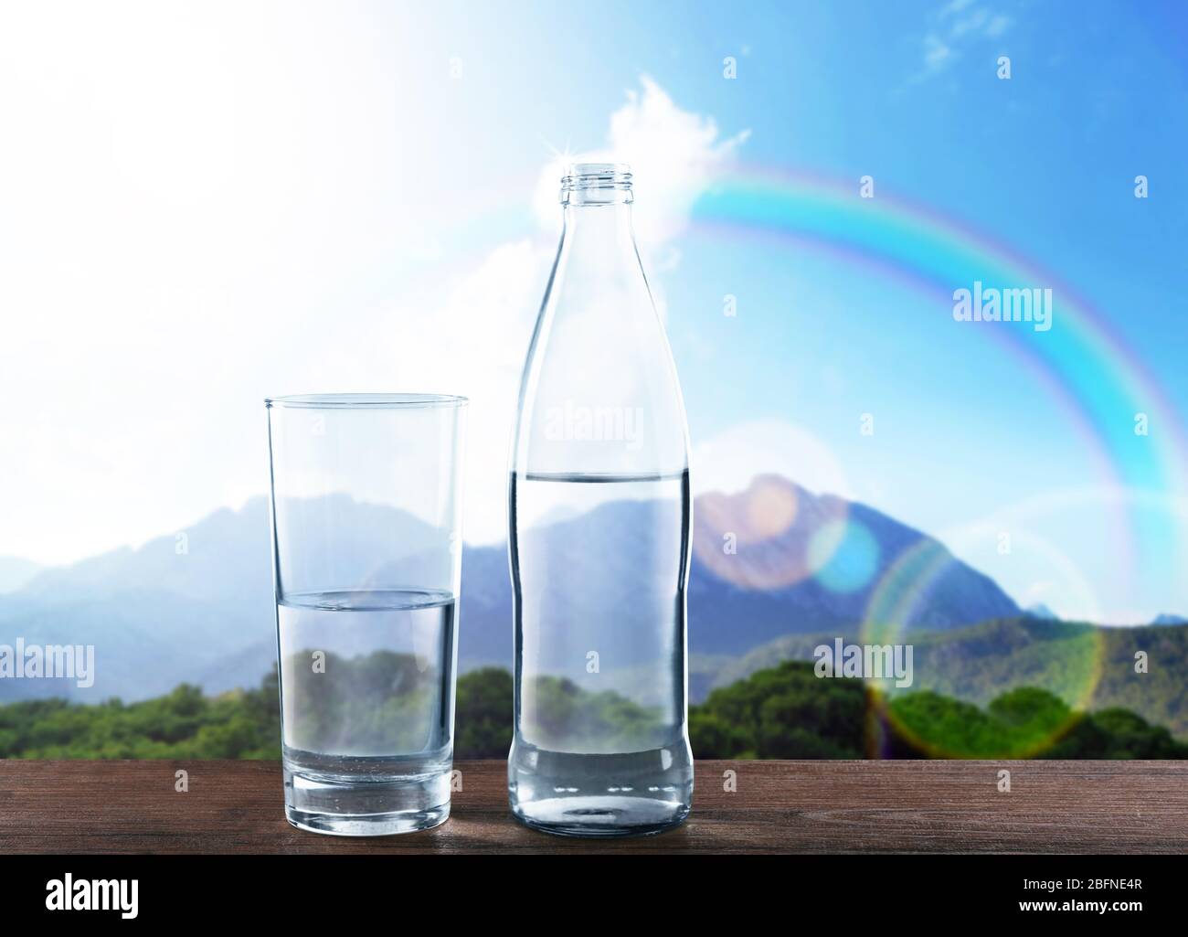 Bottle and glass of clear water on wooden table against nature background Stock Photo