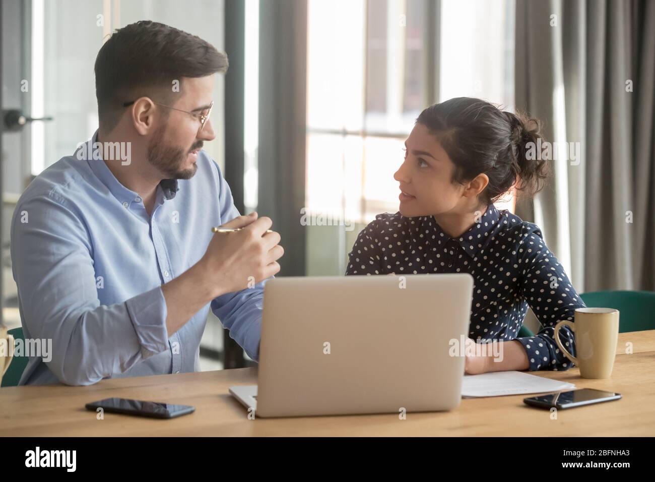 Multi-ethnic co-workers discuss project sitting at workplace Stock Photo
