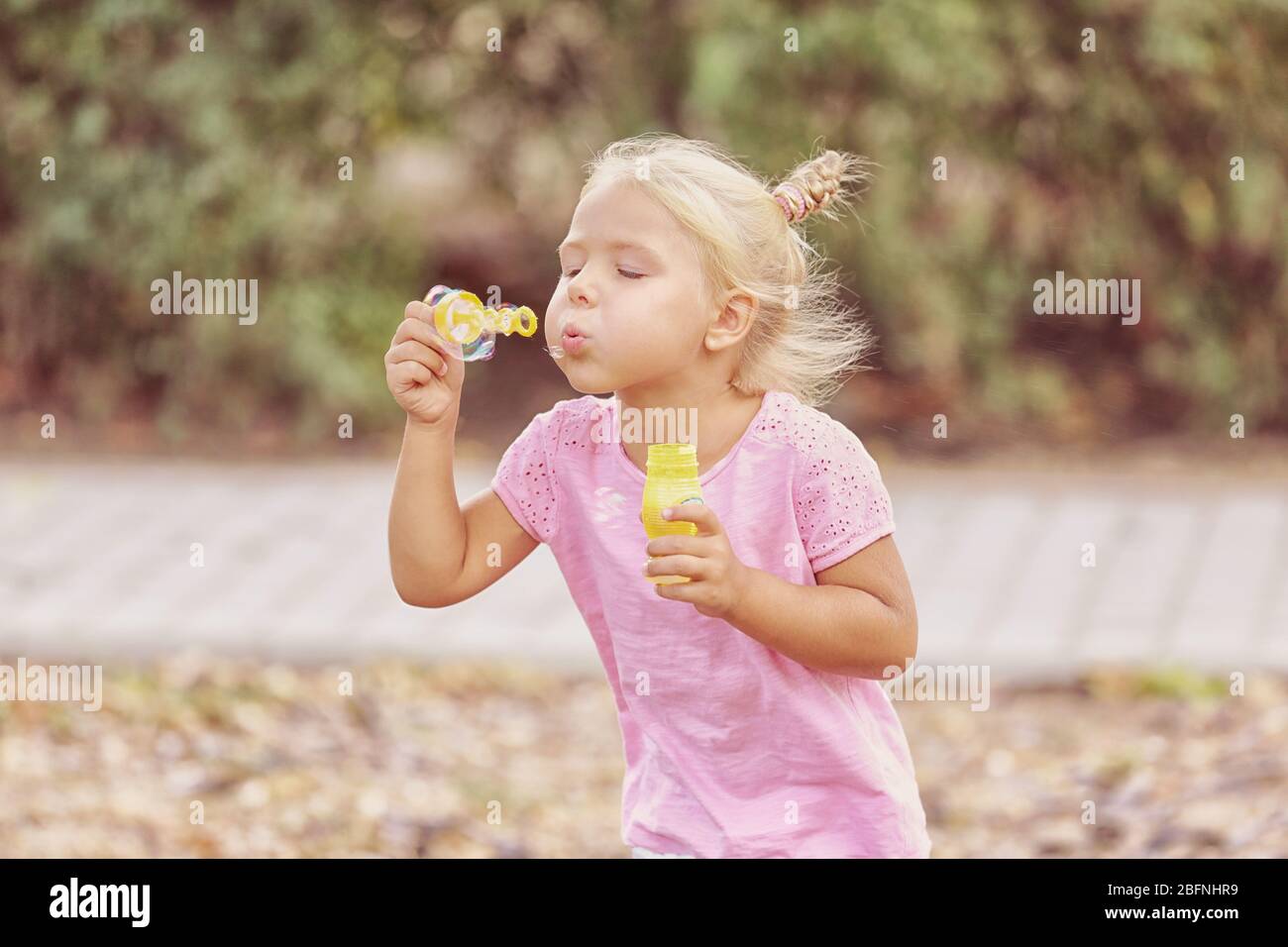Cute little girl blowing soap bubbles in park Stock Photo - Alamy