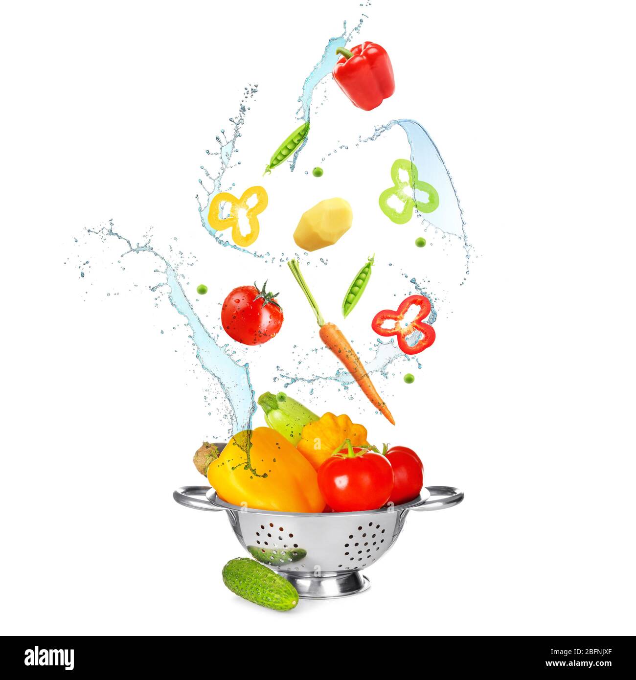 Different vegetables, water splashes and colander on white background Stock Photo