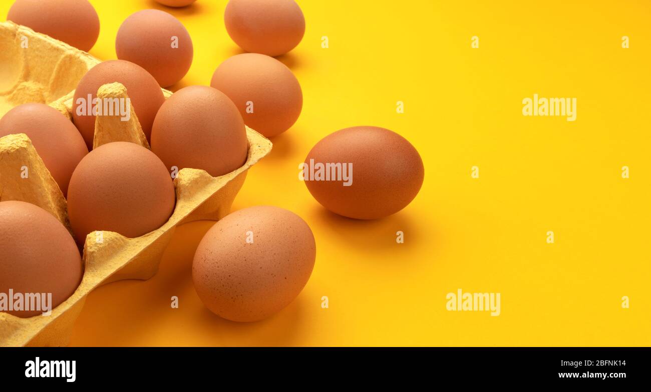 Brown chicken eggs in cardboard box on yellow background Stock Photo