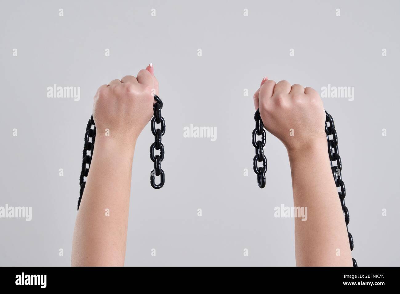 Female hands holding a broken metal chain over grey background with copy space Stock Photo