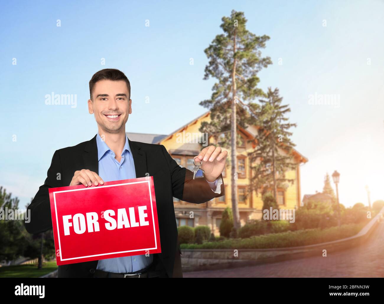 Real estate agent holding sign with text FOR SALE and key in front of ...