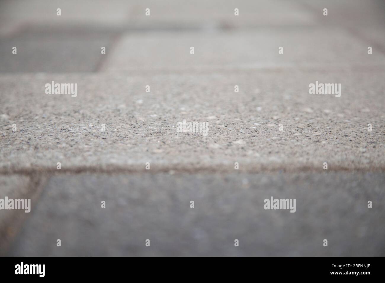 Narrow view of a concrete tile in the blurred sidewalk. Cement block on a pedestrian crossing. Textured abstract background bokeh. Stock Photo