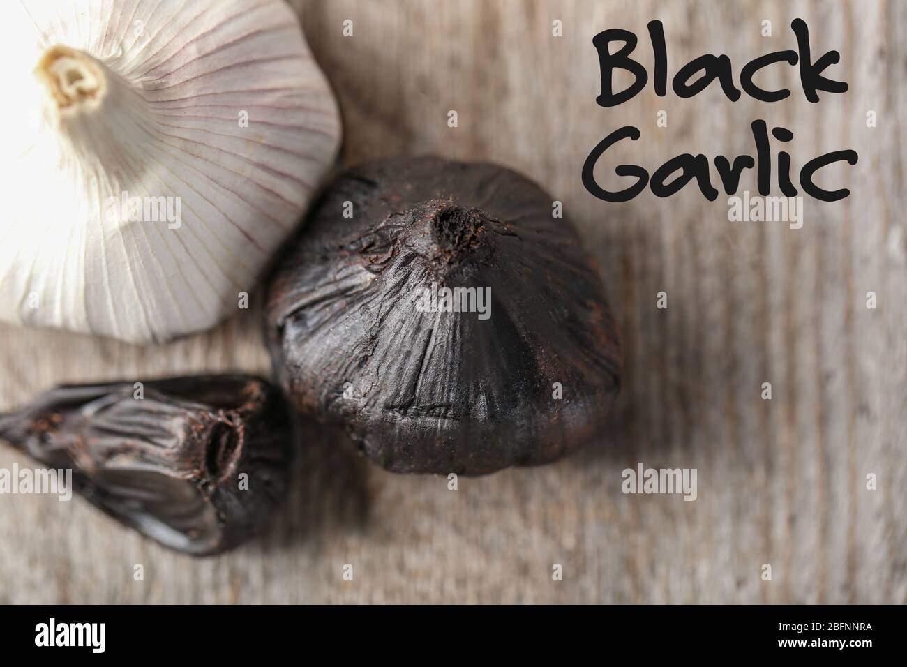 Black (Allium sativum) and white garlic bulbs on wooden table Stock Photo