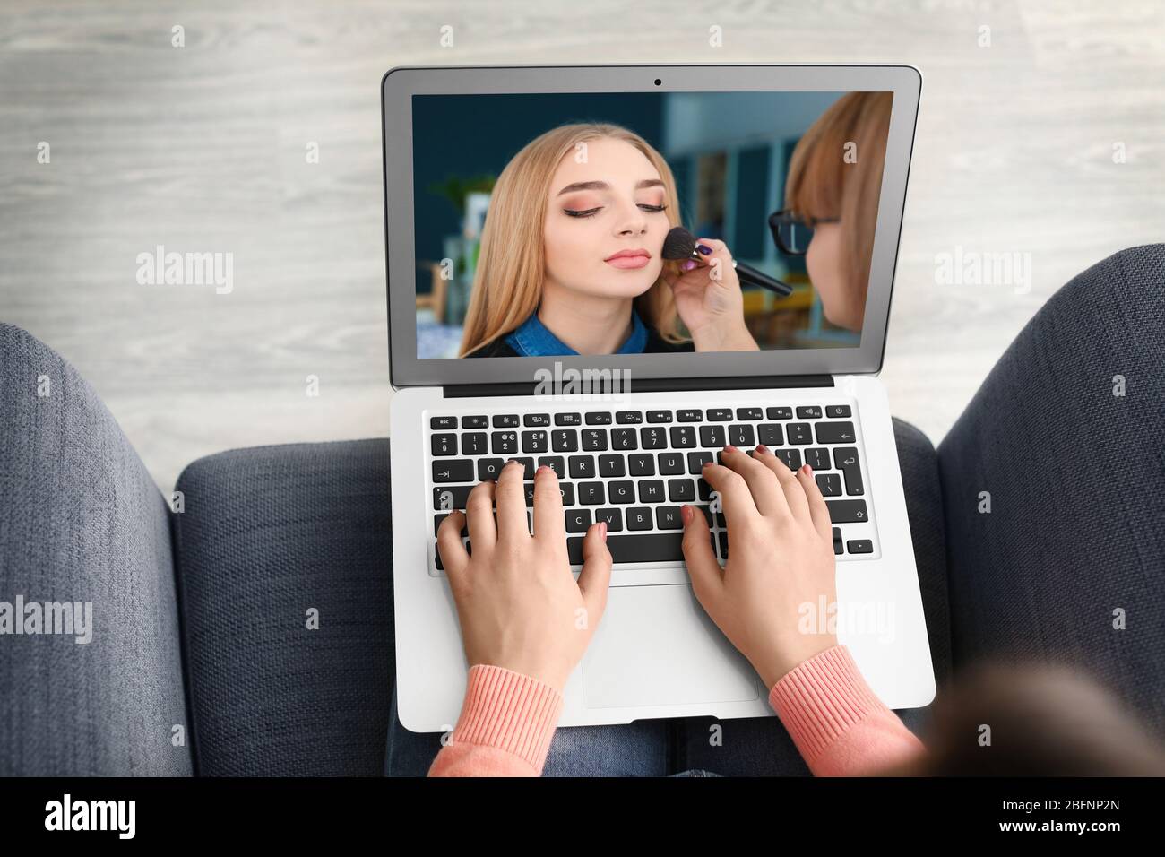 Woman sitting in armchair and watching online training for professional makeup artist on laptop Stock Photo