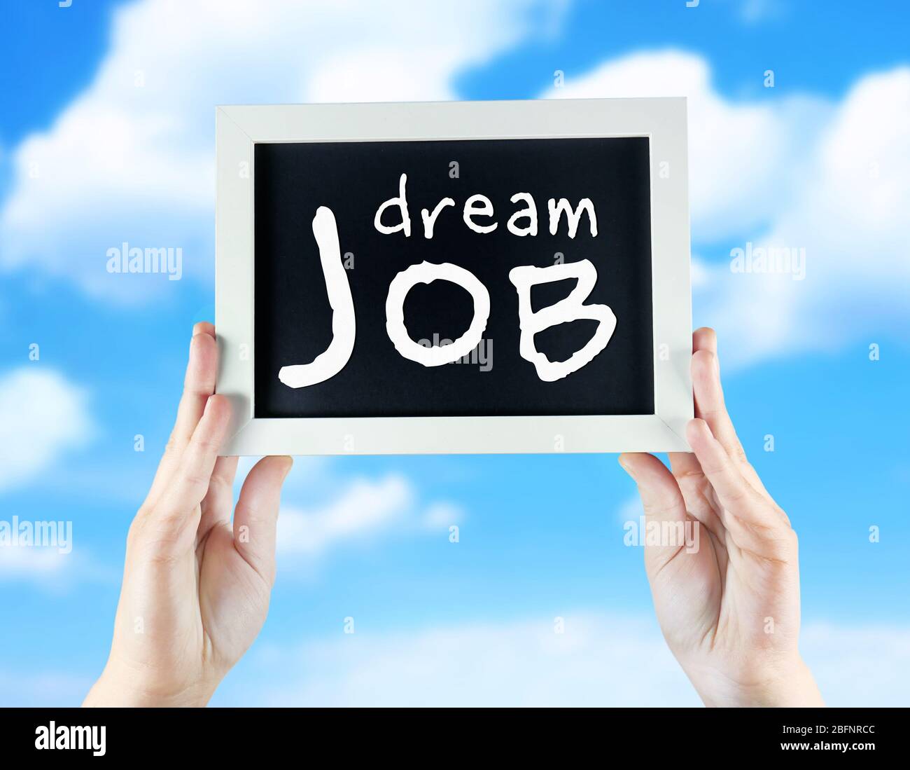 Labor market concept. Female hands holding chalkboard with text DREAM JOB on sky background Stock Photo