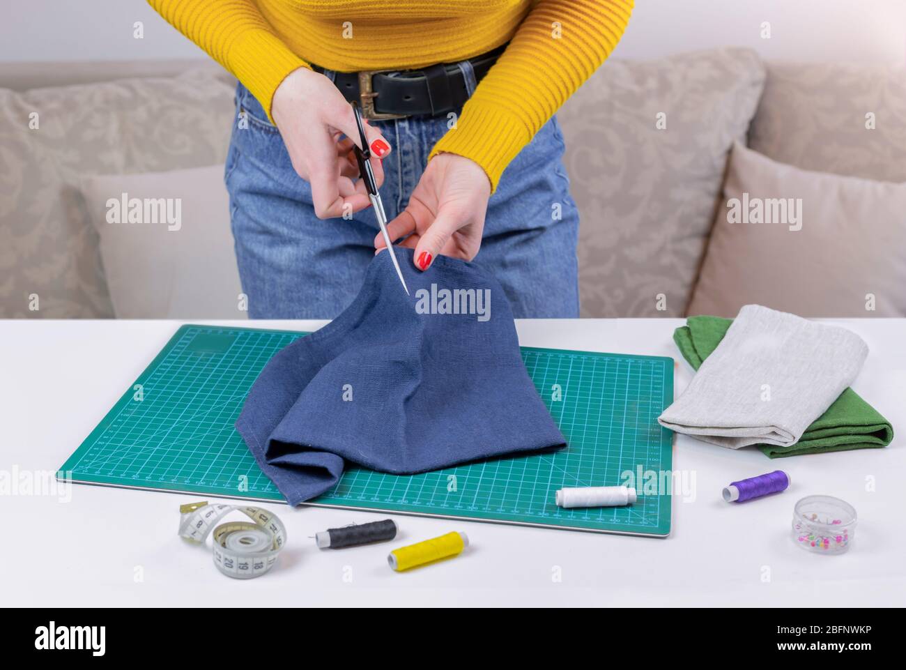 woman in a yellow cuts the fabric. there are quilting tools on the table. patchwork knife, scissors, lined cutting mat, self-locking, thread, centimet Stock Photo