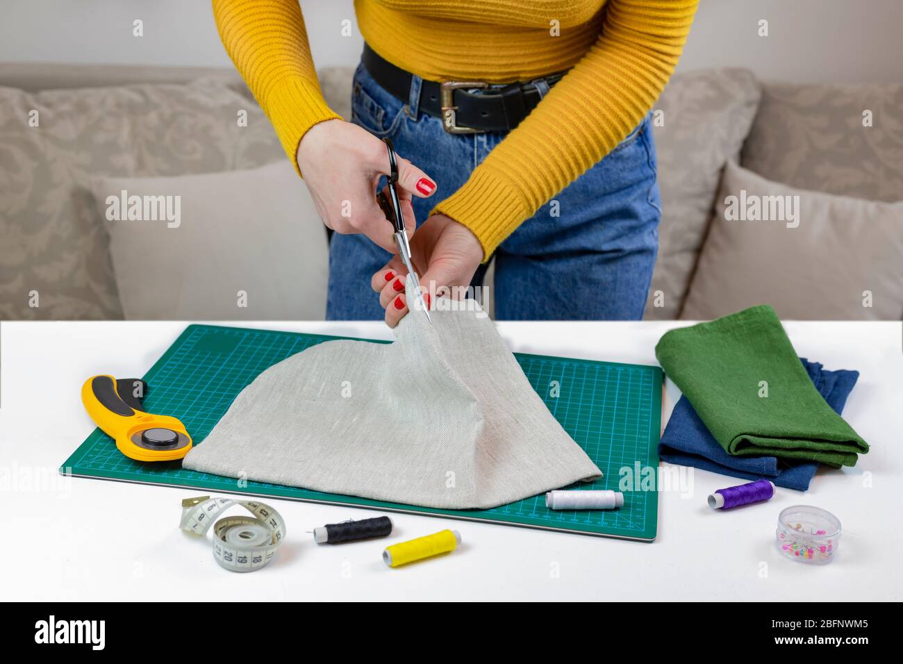 woman in a yellow cuts the fabric. there are quilting tools on the table. patchwork knife, scissors, lined cutting mat, self-locking, thread, centimet Stock Photo