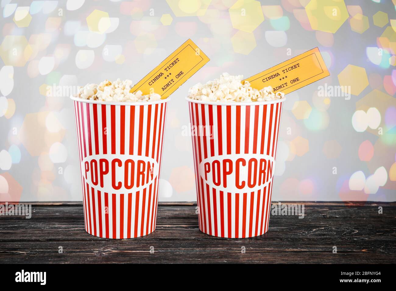 Paper cups of tasty popcorn with cinema tickets and blurred lights on ...