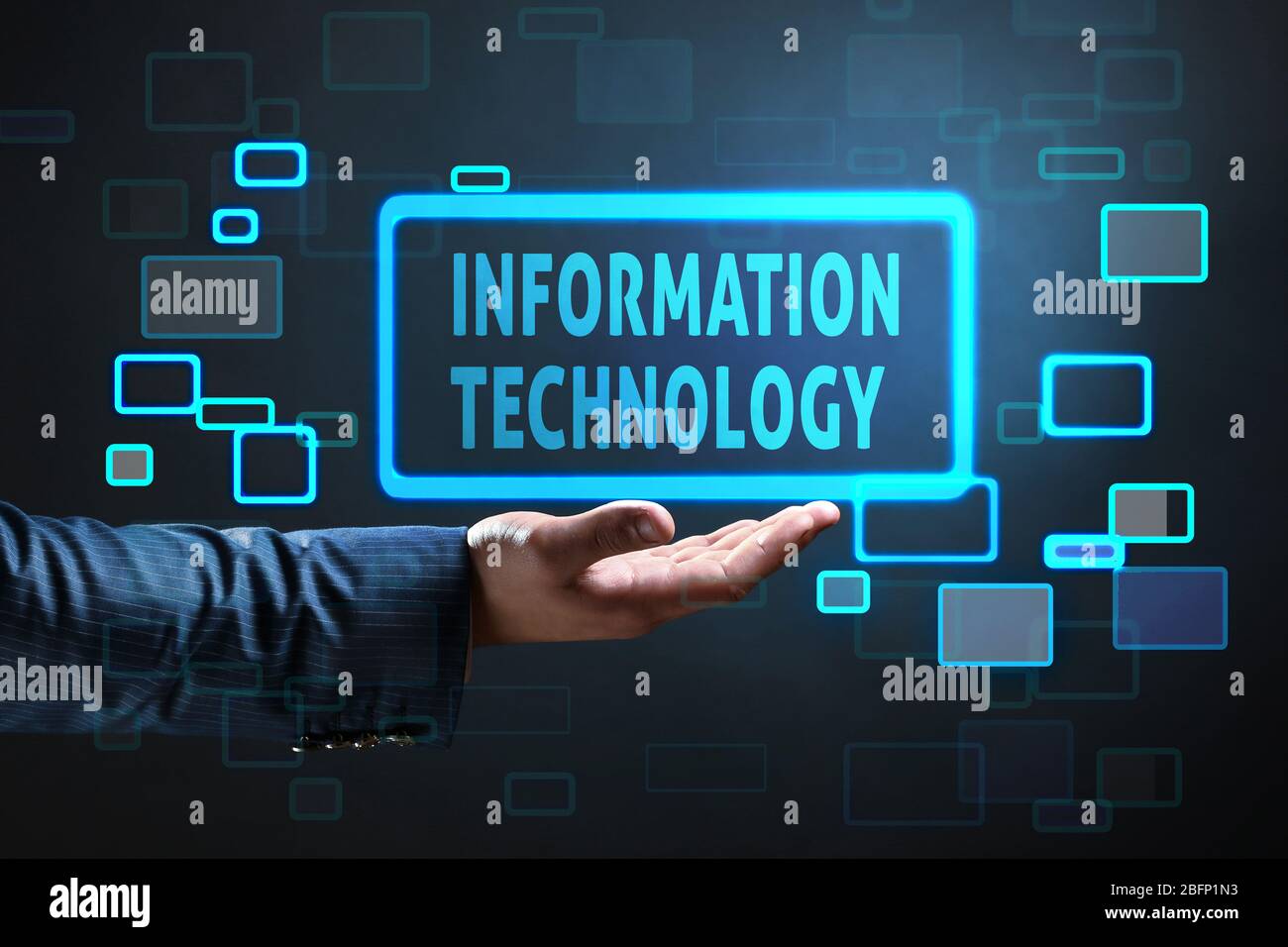 Businessman holding virtual icon with text INFORMATION TECHNOLOGY against dark background Stock Photo