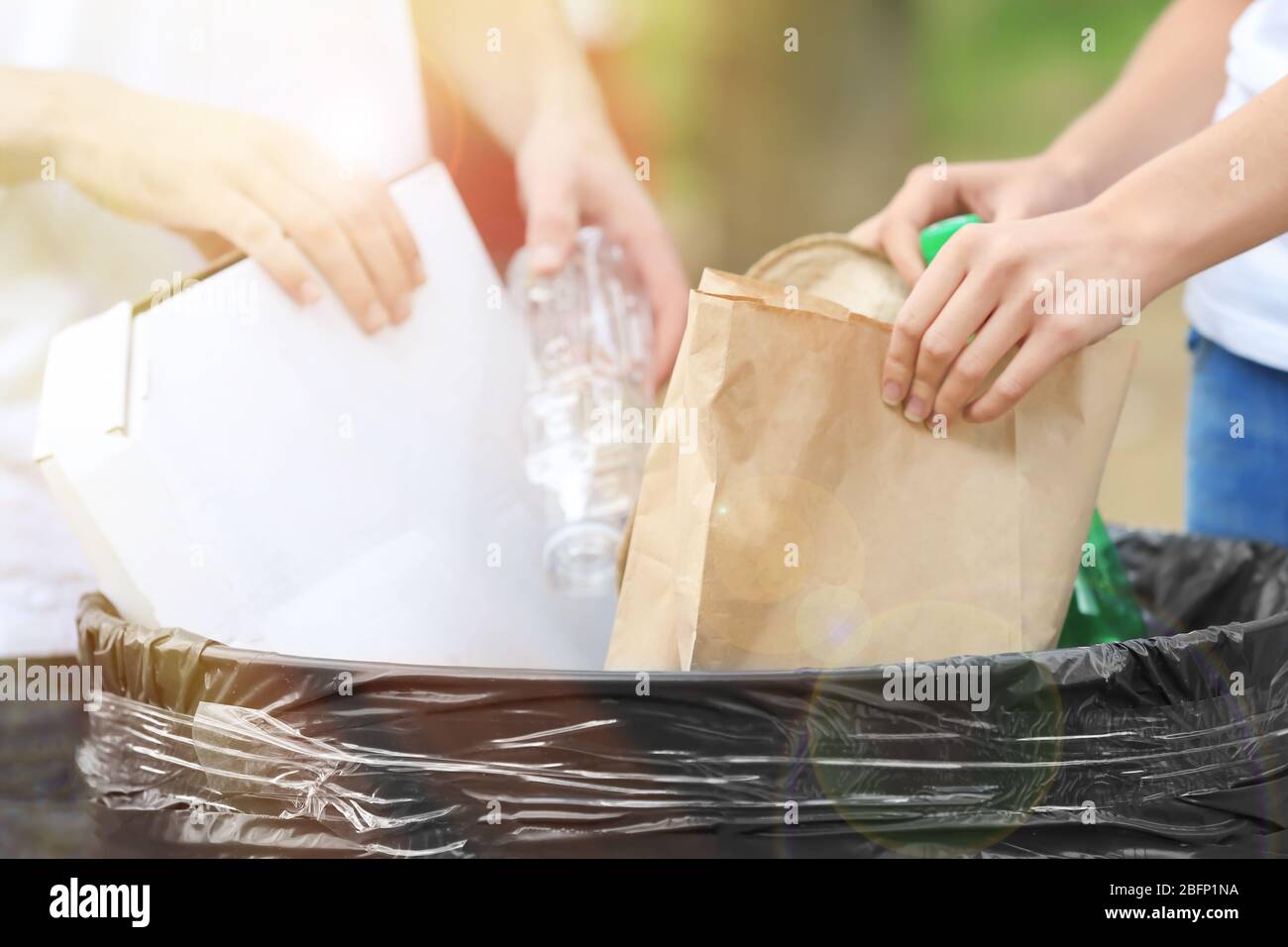 People throwing different types of garbage into litter bin outdoors, closeup. Recycling concept Stock Photo