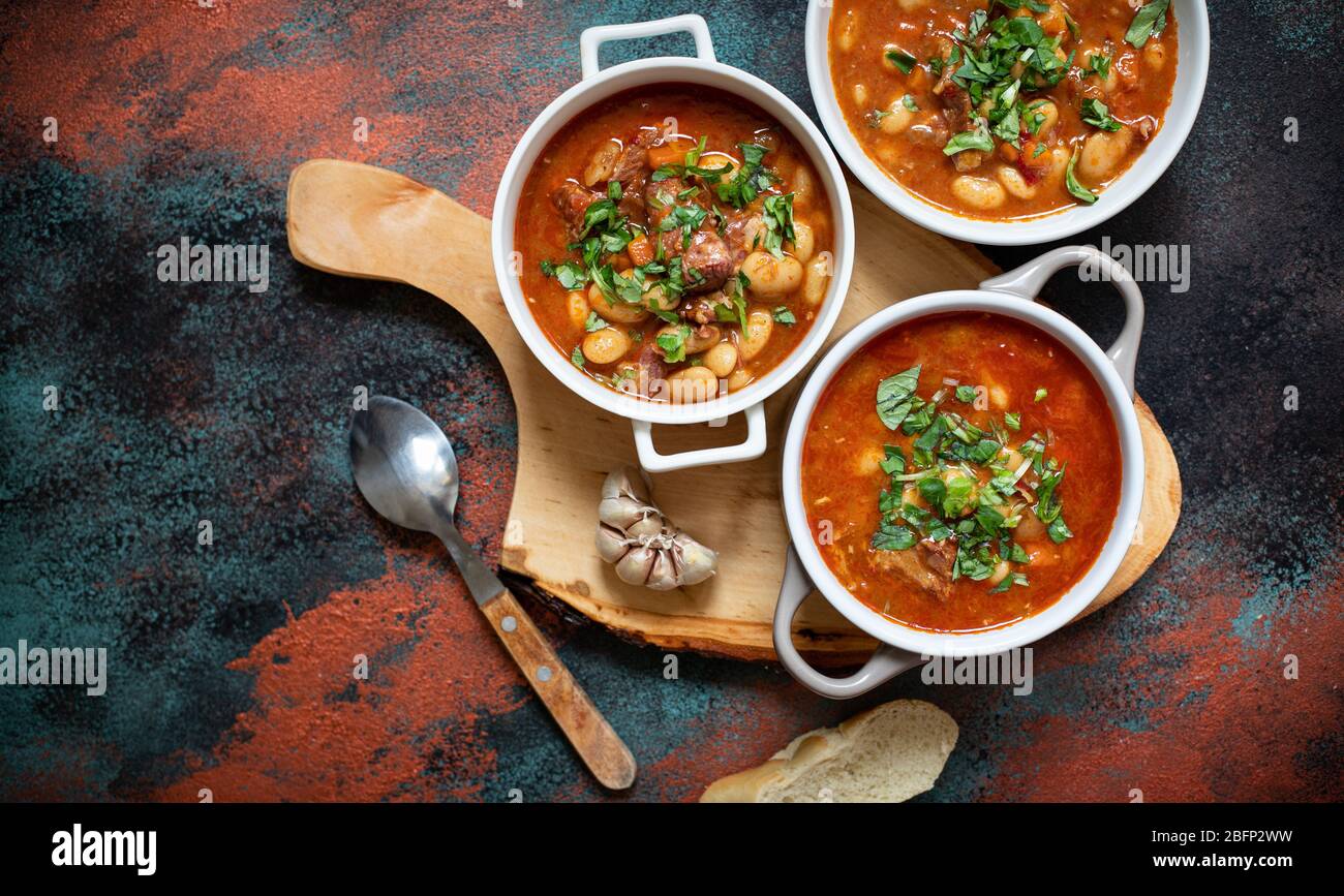 Bean soup with meat and vegetables served on a rustic board with garlic. Traditional Balkan soup or stew Corbast Pasulj (Grah) Stock Photo