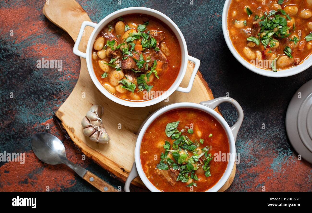 Bean soup with meat and vegetables served on a rustic board with garlic. Traditional Balkan soup or stew Corbast Pasulj (Grah) Stock Photo
