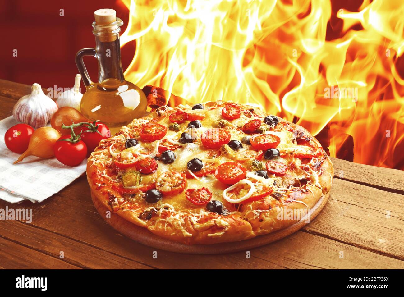 Delicious fresh pizza on wooden table against fire flame background Stock Photo