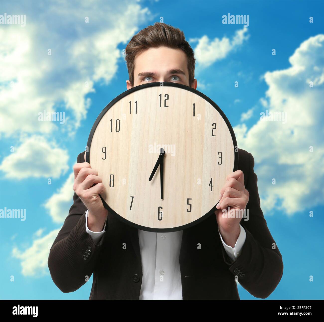 Man in black suit holding big clock on sky background Stock Photo - Alamy